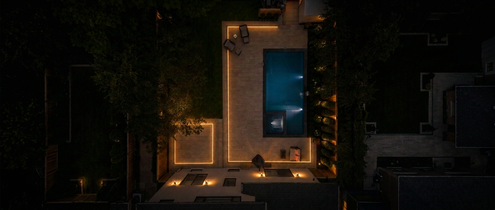 Aerial night view of a backyard pool and patio outlined with warm Zylo LED lighting